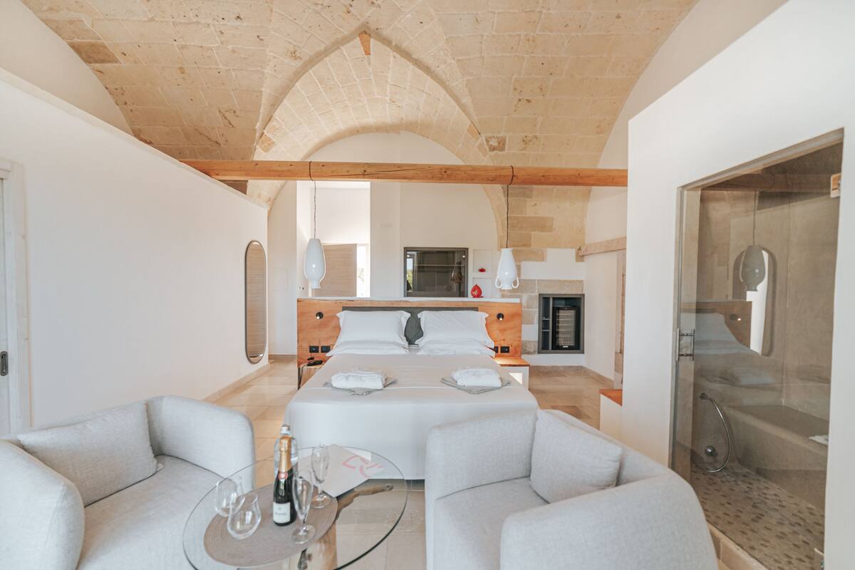 A spacious bedroom with a large bed, a sitting area with a glass table, and a shower area.