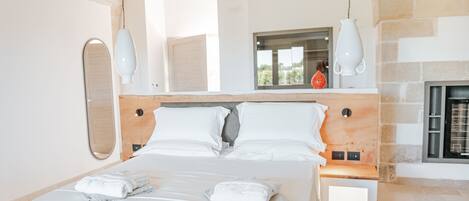 A modern bedroom with a large bed, white linens, a stone fireplace, and hanging pendant lights.