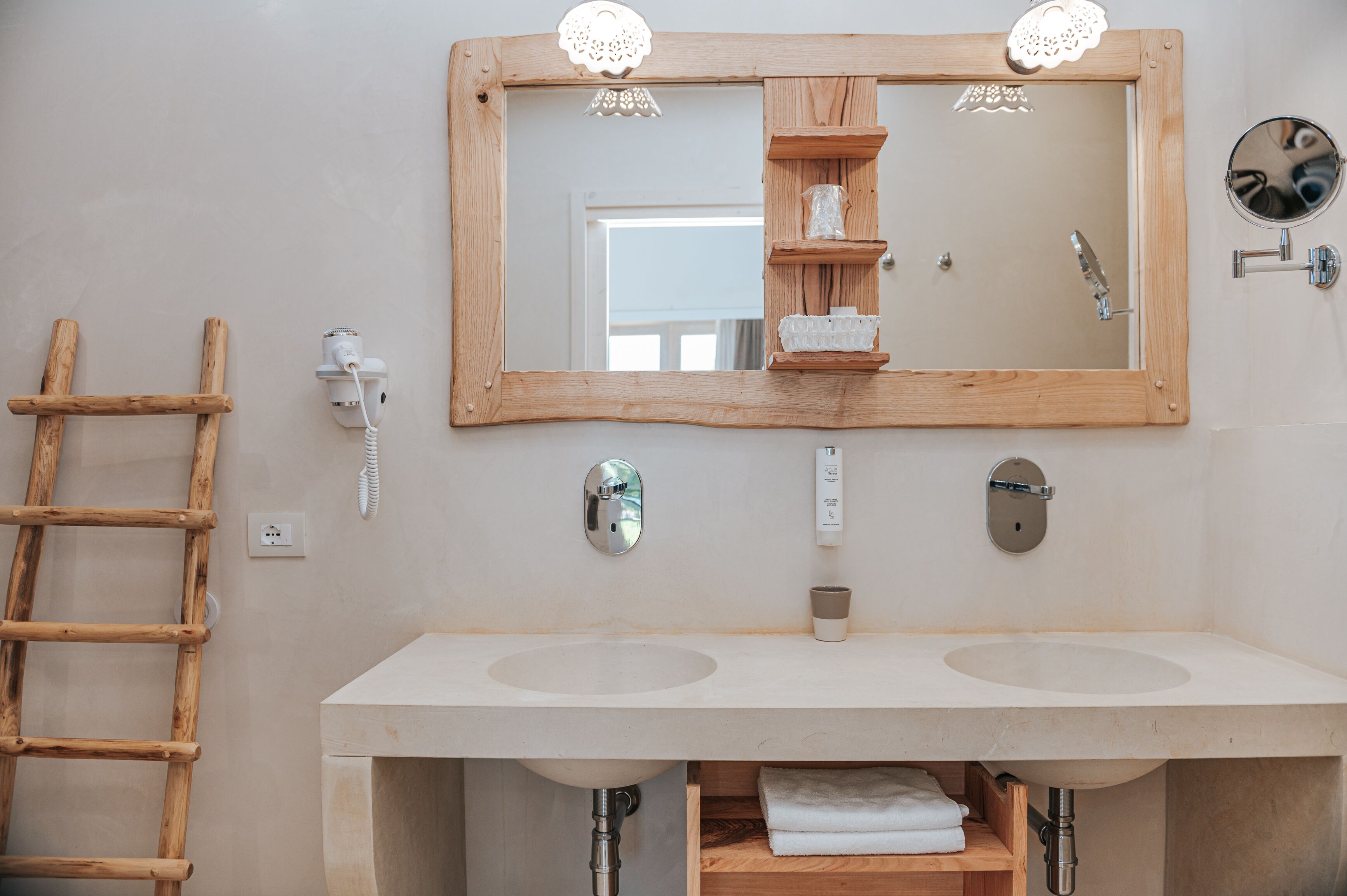 A bathroom with two sinks, a wooden-framed mirror, a towel rack, and a wooden shelf.