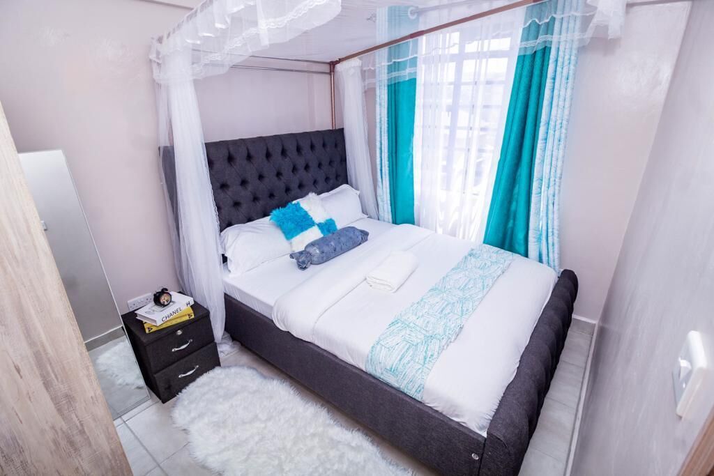 A bedroom with a bed, a nightstand, a mirror, and a window with curtains.