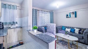 Un espacio habitable compacto con kitchenette, un sofá gris, una mesita de centro pequeña y un adorno de pared.