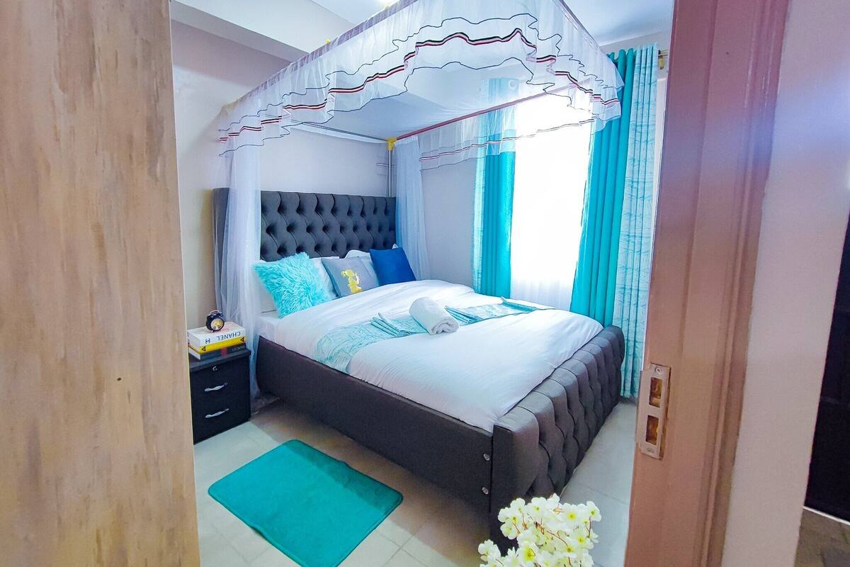 A bedroom with a four-poster canopy bed, a bedside table with a lamp, and a green mat on the floor.