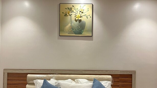 Ein ordentlich bezogenes Bett mit weißen Leinen und blauen Kissen, ein hölzerner Kopfteil und ein Blumenbild an der Wand.