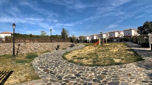 A paved pathway leading to a playground with a slide, surrounded by buildings with red-tiled roofs. - Preciosa Casa Rural en El Ronquillo (El Ronquillo)