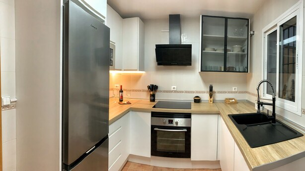 A compact kitchen with a built-in oven, a stainless steel refrigerator, a microwave, and a sink. - Preciosa Casa Rural en El Ronquillo (El Ronquillo)