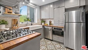 A modern kitchen with stainless steel appliances, a wooden countertop, and patterned tile flooring.