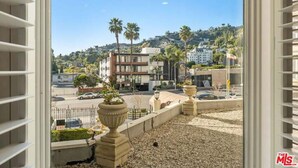 A view from a window overlooking a street with buildings, palm trees, and a parking area.