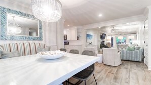 A spacious living area with a large dining table, a chandelier, and a seating area with a sofa and chairs. - 302 Charleston by AvantStay | Stunning Private Pool (Isle Of Palms)