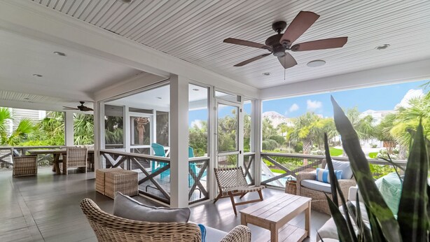 A spacious indoor area with wicker furniture, a ceiling fan, and large windows offering a view of a pool and greenery. - 302 Charleston by AvantStay | Stunning Private Pool (Isle Of Palms)