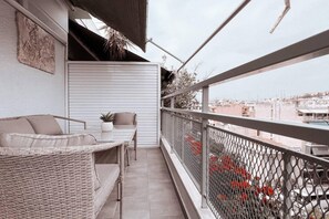 A balcony with a wicker sofa, a small table, and a potted plant. - Penthouse - Amazing View in the Center of Athens (Athens)