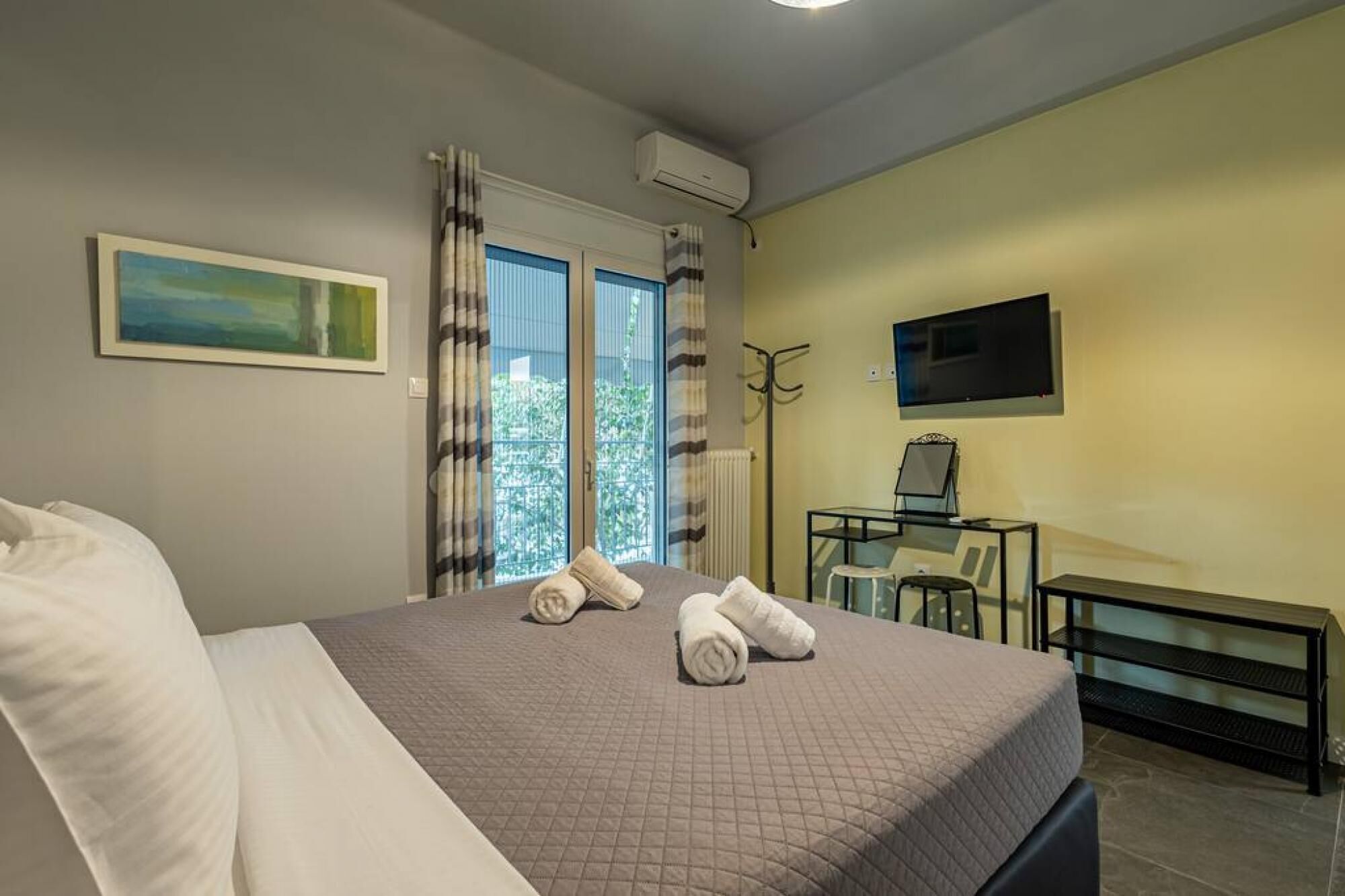 A bedroom with a bed, a desk, a chair, a TV, and a window with curtains.