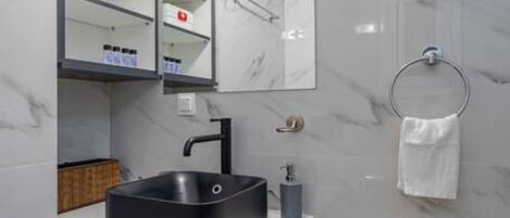 A modern bathroom with a black sink, white marble walls, a large mirror, and a white laundry basket.