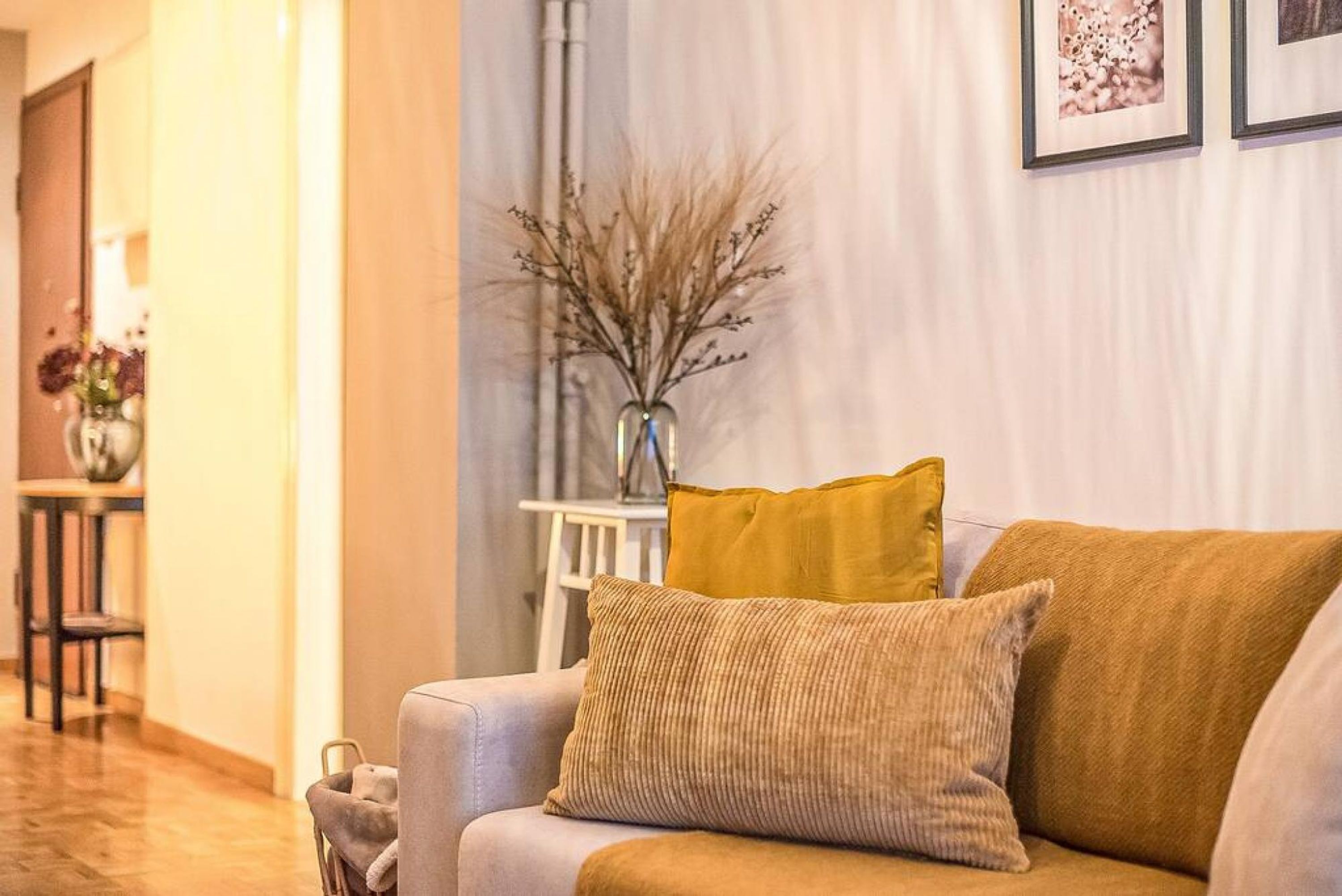 Ein Wohnzimmer mit einer Couch, einer Vase mit getrockneten Pflanzen und gerahmten Bildern an der Wand.