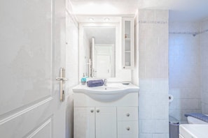 A bathroom with a white sink, mirror, and cabinets.