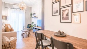 A modern living room with a wooden dining table, black chairs, and a chandelier. There are framed pictures on the wall and a basket on the floor. - Bohemian Chic 1BR Apartment in the Heart of Athens (Athens)