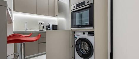 A compact kitchen with a built-in washing machine and oven, a sink, and a red bar stool.