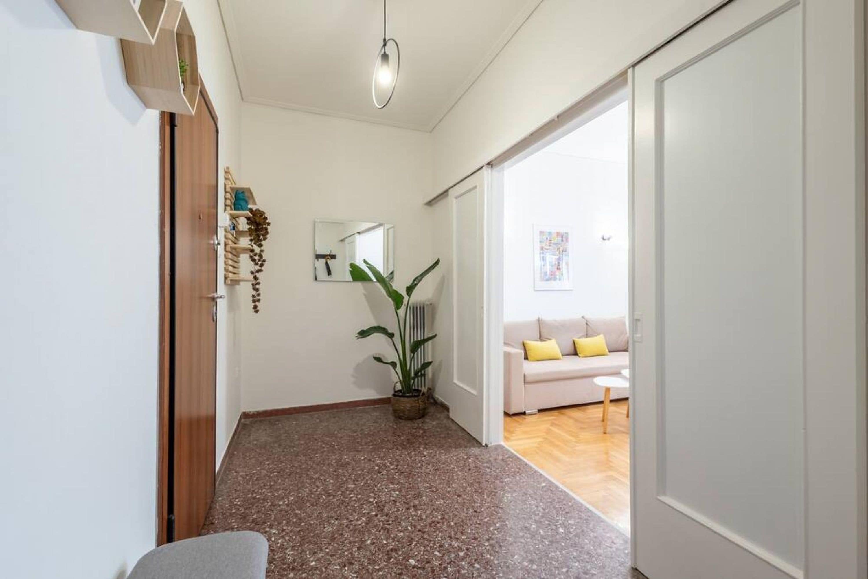Ein Korridor mit einem Blumentopf, einem weißen Sofa mit gelben Kissen und einer Holztür.