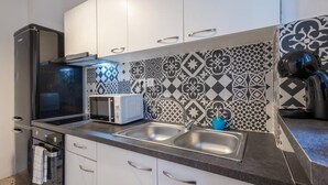 A modern kitchen with white cabinets, a black refrigerator, a microwave, and a sink. - Roubnb Acropolis Museum 1BD Apt (Athens)