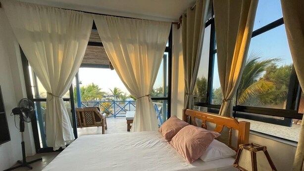 Une chambre à coucher avec un lit, des rideaux, une tête de lit en bois, une lampe de chevet et une vue sur l’extérieur.