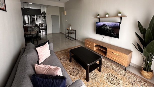 A modern living room with a grey sofa, black coffee table, wooden TV stand, and a patterned rug. - Ideal choice for those seeking transit convenience to and from KLIA (Sepang)