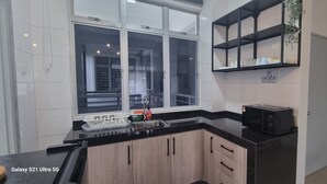 A modern kitchen with a black countertop, a microwave, a sink, and a window with a view of the outside. - Ideal choice for those seeking transit convenience to and from KLIA (Sepang)