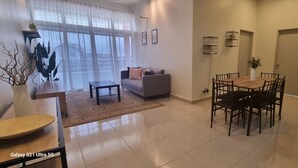 A modern living room with a sofa, a dining table with chairs, and a large window with sheer curtains. - Ideal choice for those seeking transit convenience to and from KLIA (Sepang)