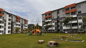 A playground with slides and swings, surrounded by apartment buildings with balconies and a grassy area. - Ideal choice for those seeking transit convenience to and from KLIA (Sepang)