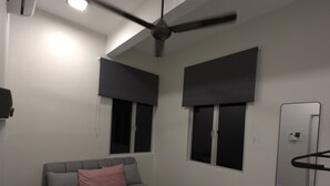 A modern bedroom with a bed, a ceiling fan, and two windows with dark blinds. - Ideal choice for those seeking transit convenience to and from KLIA (Sepang)