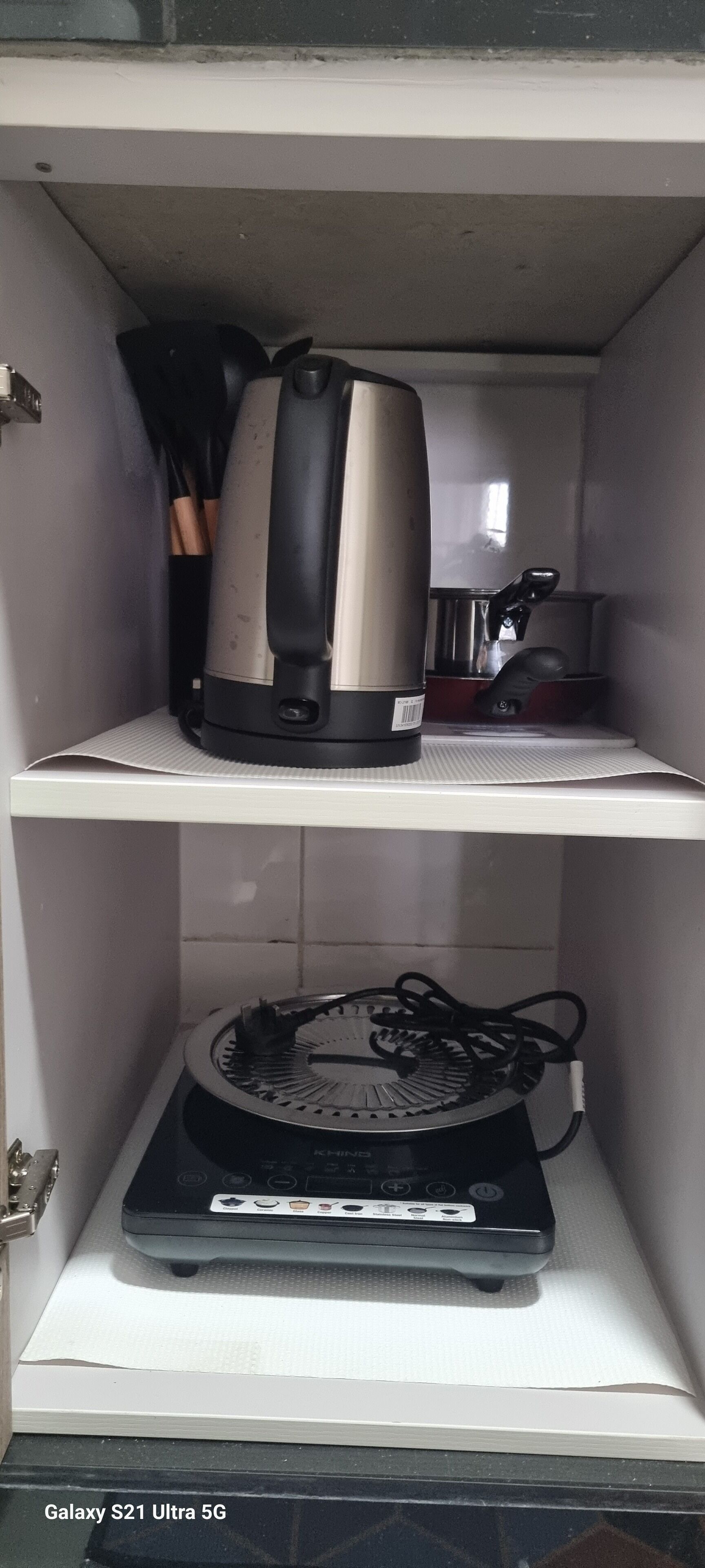 A kitchen with a kettle and a rice cooker on the shelves.