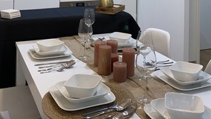 Una cucina moderna con mobili bianchi, un piano di lavoro nero e un'area pranzo apparecchiata con piatti, bicchieri e posate bianche.