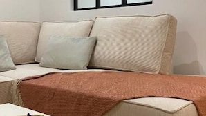 Un soggiorno con un divano color beige, un tavolino in legno e un'ampia finestra con cornici nere.