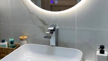 A bathroom with a white sink, a round mirror with a light, and a wooden countertop.