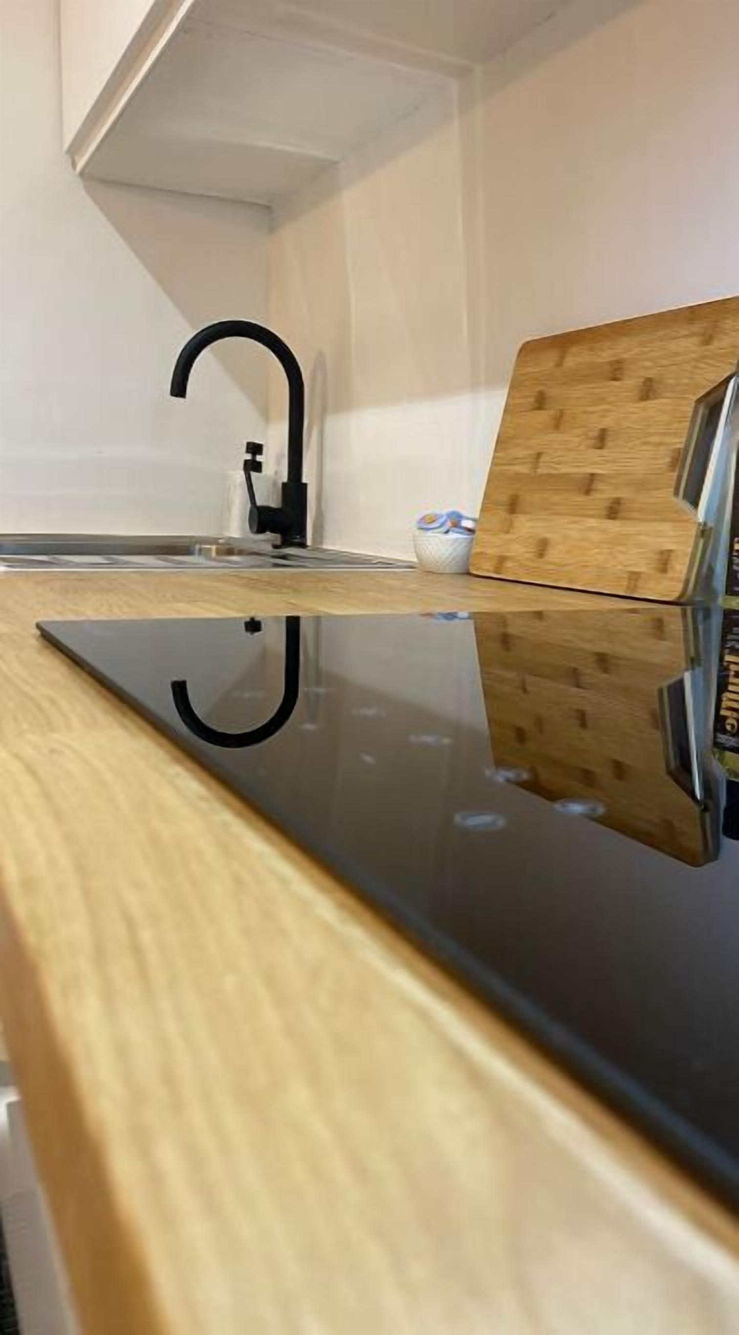 A kitchen with a black countertop, a wooden cutting board, and a black faucet.