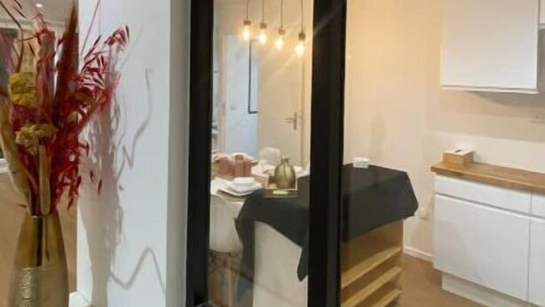 Un interno moderno con una grande finestra, un divano bianco, un angolo cottura e un vaso con fiori rossi su un davanzale.