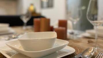 Une table à manger dressée avec de l’assiette blanche, des bols et des couverts en argent, et un set de table en fibres naturelles placé en dessous.