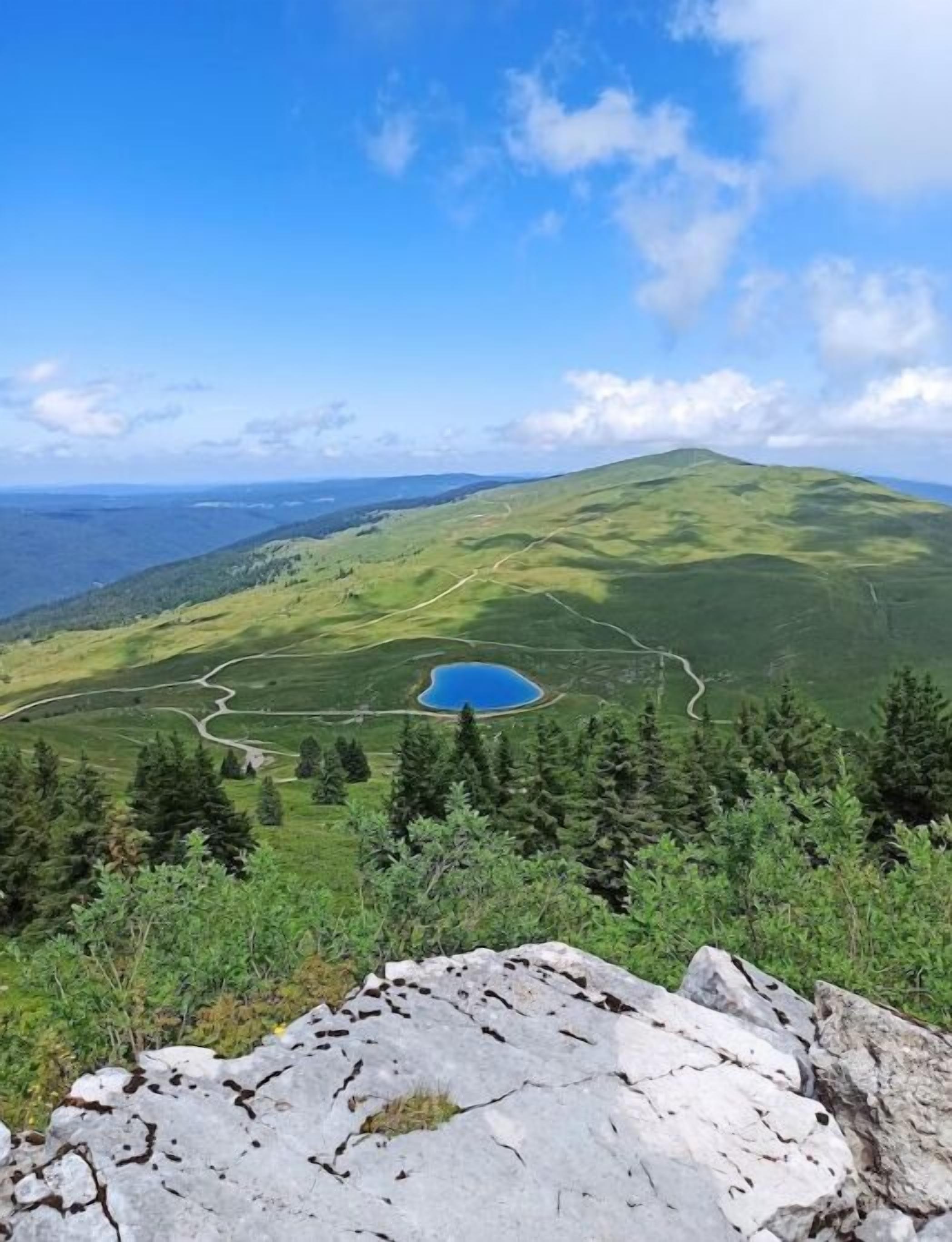 Paesaggio montuoso con un lago blu cristallino circondato da vegetazione e un sentiero sinuoso.