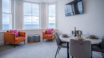 Un comedor moderno con una mesa redonda, dos sillones naranja y un amplio ventanal con vistas al mar.