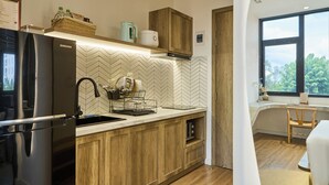 Une cuisine moderne dotée d’un réfrigérateur encastré, de meubles en bois, d’un dosseret en carreaux disposés en motif chevron et d’une fenêtre offrant une vue sur la verdure environnante.