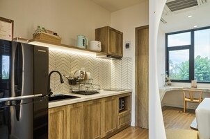 Uma cozinha moderna com frigorífico embutido, armários de madeira, painel de azulejos em padrão herringbone e uma janela com vista para o verde lá fora.