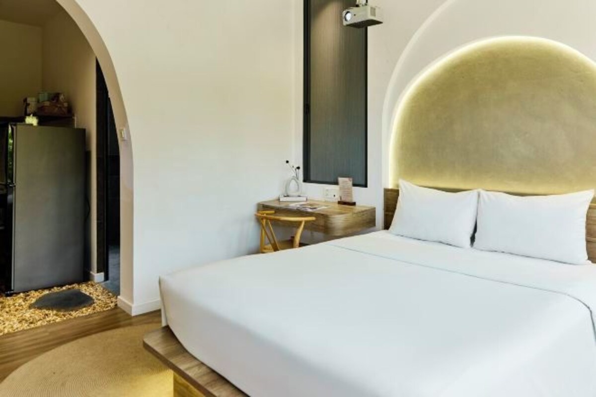 Ein modernes Hotelzimmer mit einem großen Bett, einem kleinen Nachttisch mit Lampe und einer außergewöhnlichen, runden Leuchte über dem Bett.