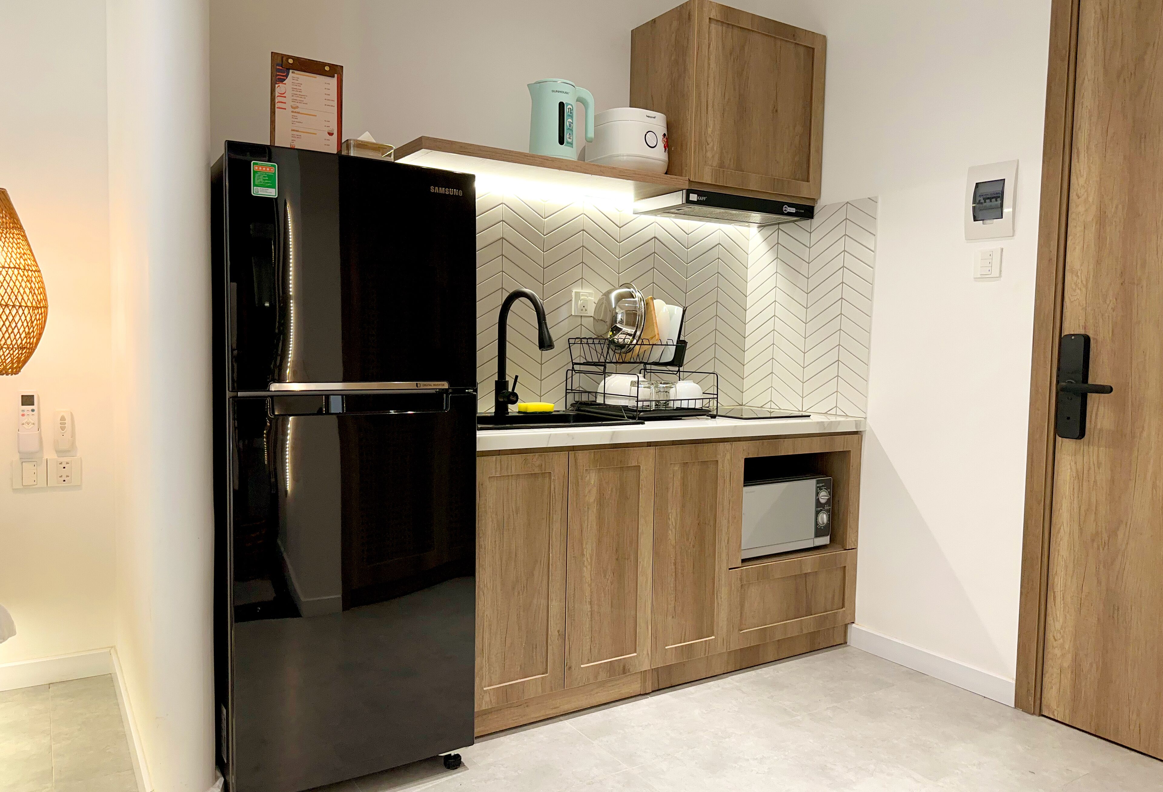 A modern kitchen with a black refrigerator, wooden cabinets, a microwave, and a kettle on the countertop.