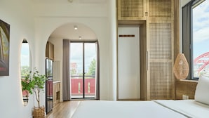 Une chambre d’hôtel moderne avec un grand lit, une vue sur la ville et un balcon agrémenté d’une structure rouge en arrière-plan.