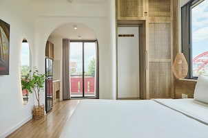 Quarto de hotel moderno com uma cama grande, vista para a cidade e uma varanda com uma estrutura vermelha ao fundo.