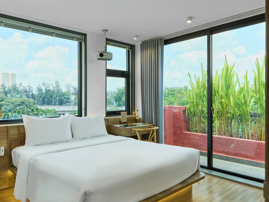 Habitación de hotel moderna con una cama grande, un escritorio y vistas a zonas verdes y edificios.