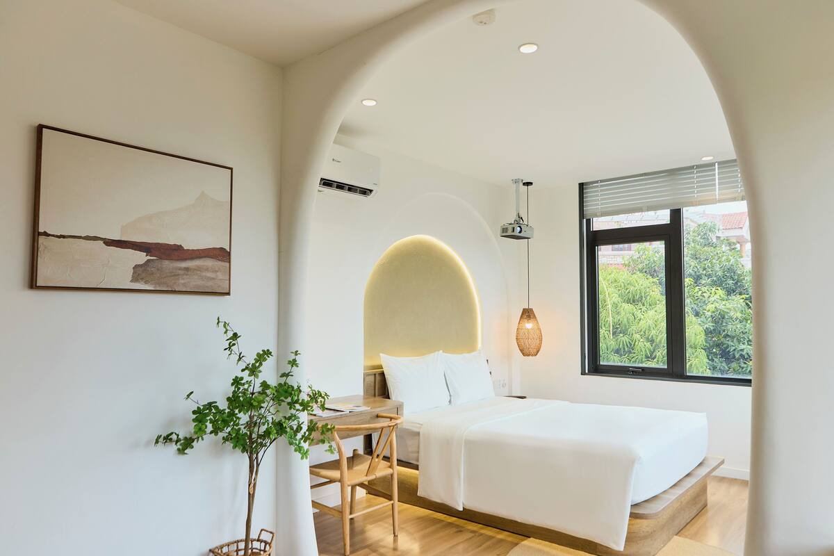 A modern bedroom with a bed, a desk, and a plant.