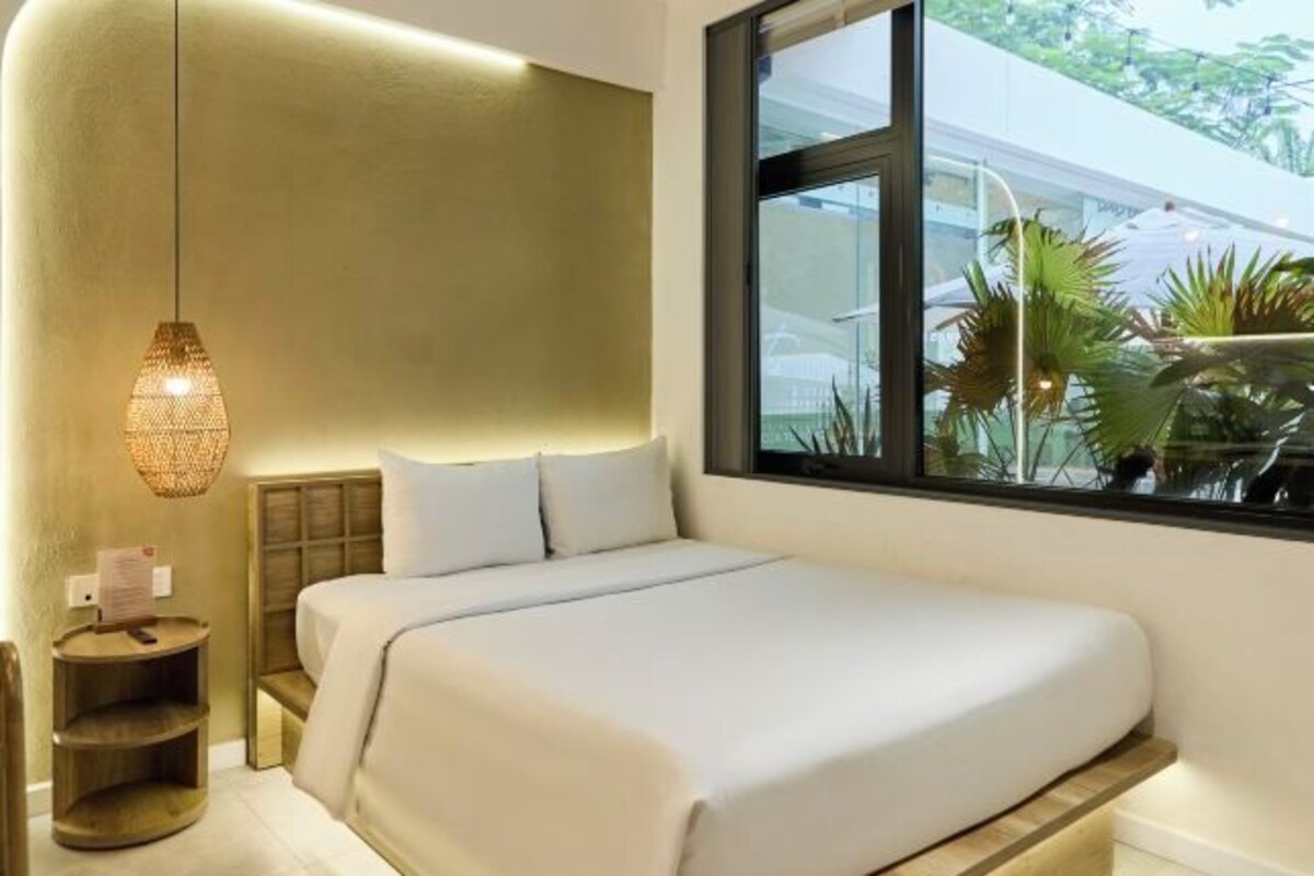 Une chambre moderne avec un lit, des tables de chevet, un luminaire suspendu et une fenêtre donnant sur un paysage verdoyant.