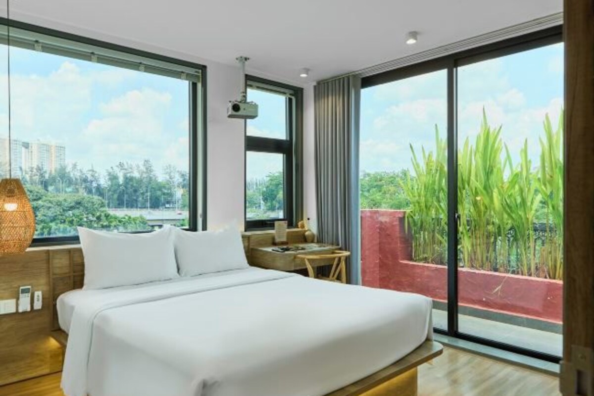 Une chambre d’hôtel moderne avec un grand lit, un bureau et une vue sur la verdure et les bâtiments.