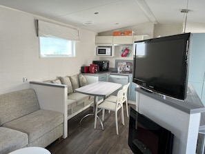 A compact kitchenette with a microwave, toaster, and coffee maker. There is a dining area with a table and chairs, and a sofa. - Mobilhome Ra30 Camping 4 Vias Plage 6/8 Personnes (Vias)