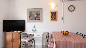 A compact living space with a flat-screen TV, a dining table with a fruit bowl, and two paintings on the wall. - Nice apartment on the first floor with a covered balcony (Baska)