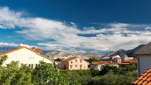 A residential area with houses, some with red-tiled roofs, and mountains in the background. - Nice apartment on the first floor with a covered balcony (Baska)